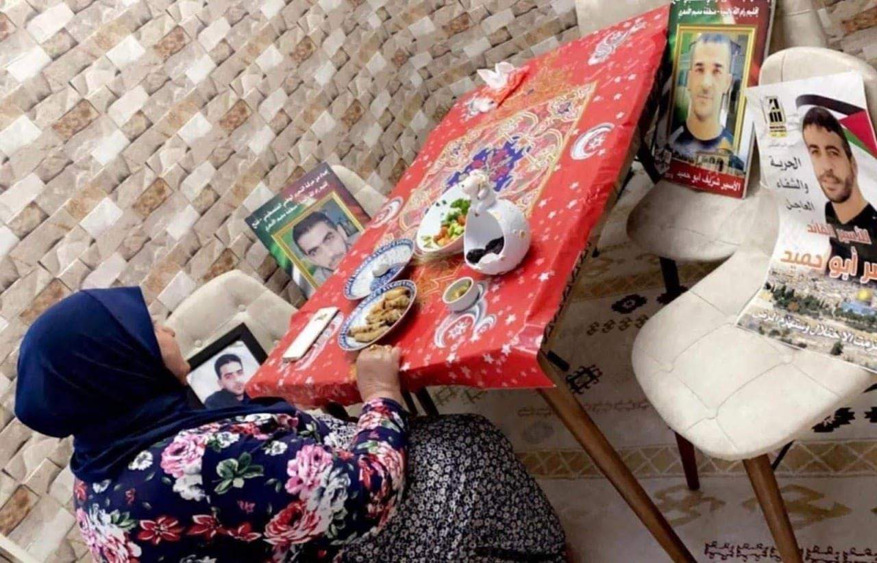بالصور ـ أم فلسطينية تستأنس بصور أبنائها الأسرى على مائدة الإفطار .. لم تجتمع بهم منذ 35 عامًا